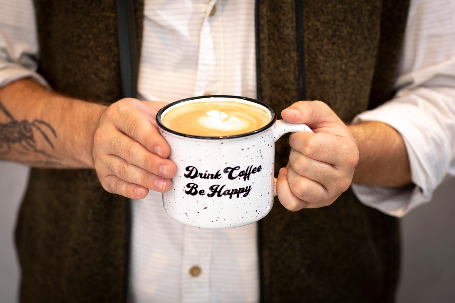 Photograph of an Austin Java patron holding a cup of coffee that reads "Drink Coffee Be Happy"