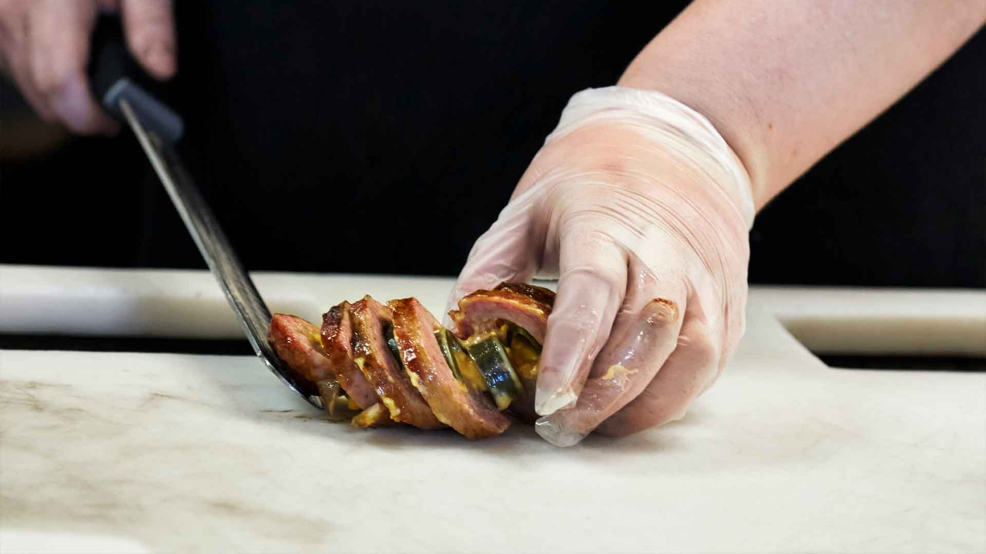 Mout-watering food photography of a line cook slicing up a delicious sausage slammer from Southside Market & Barbeque